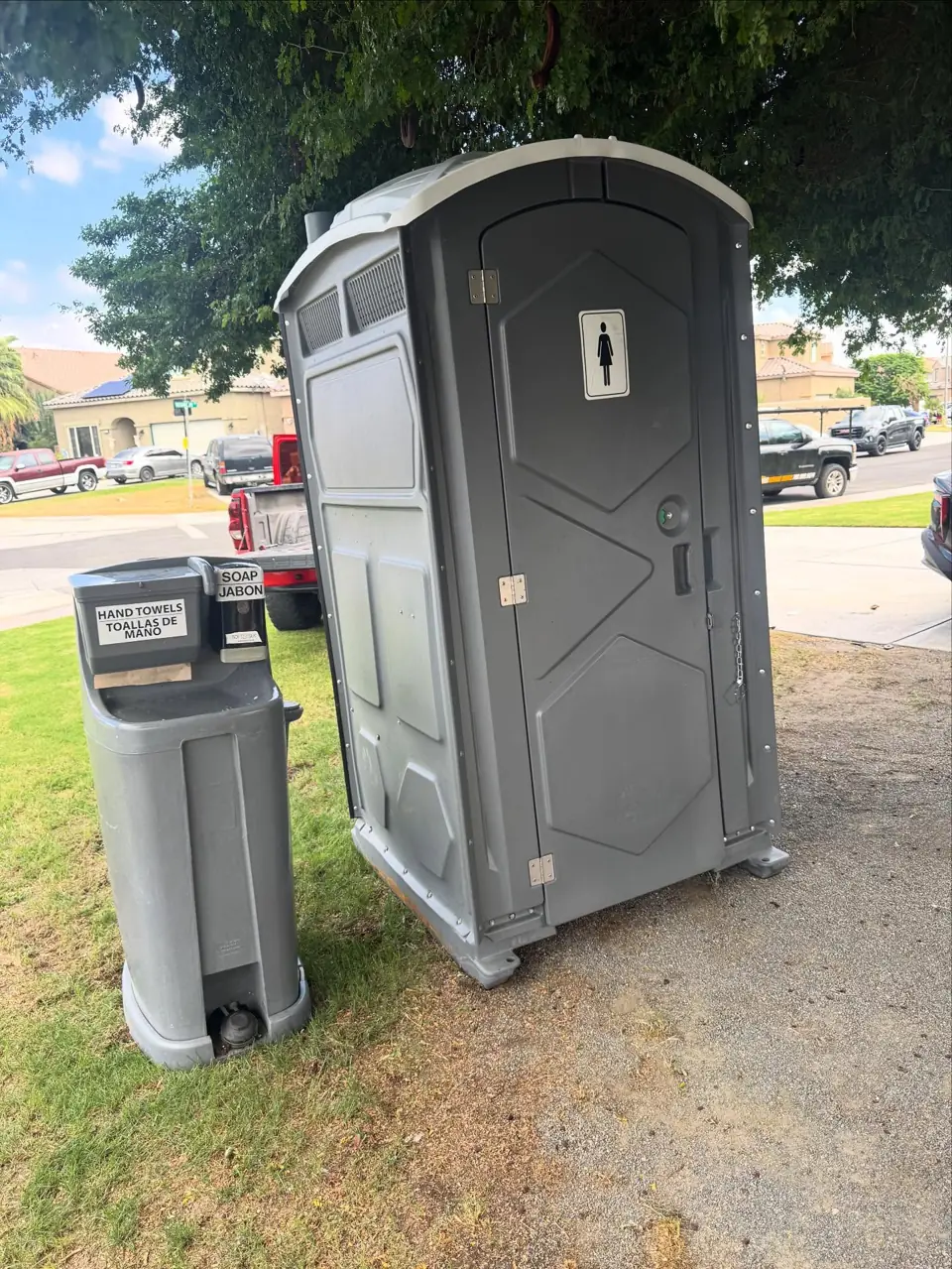 Gray portable toilet with a foot-pump hand washing station on a lawn