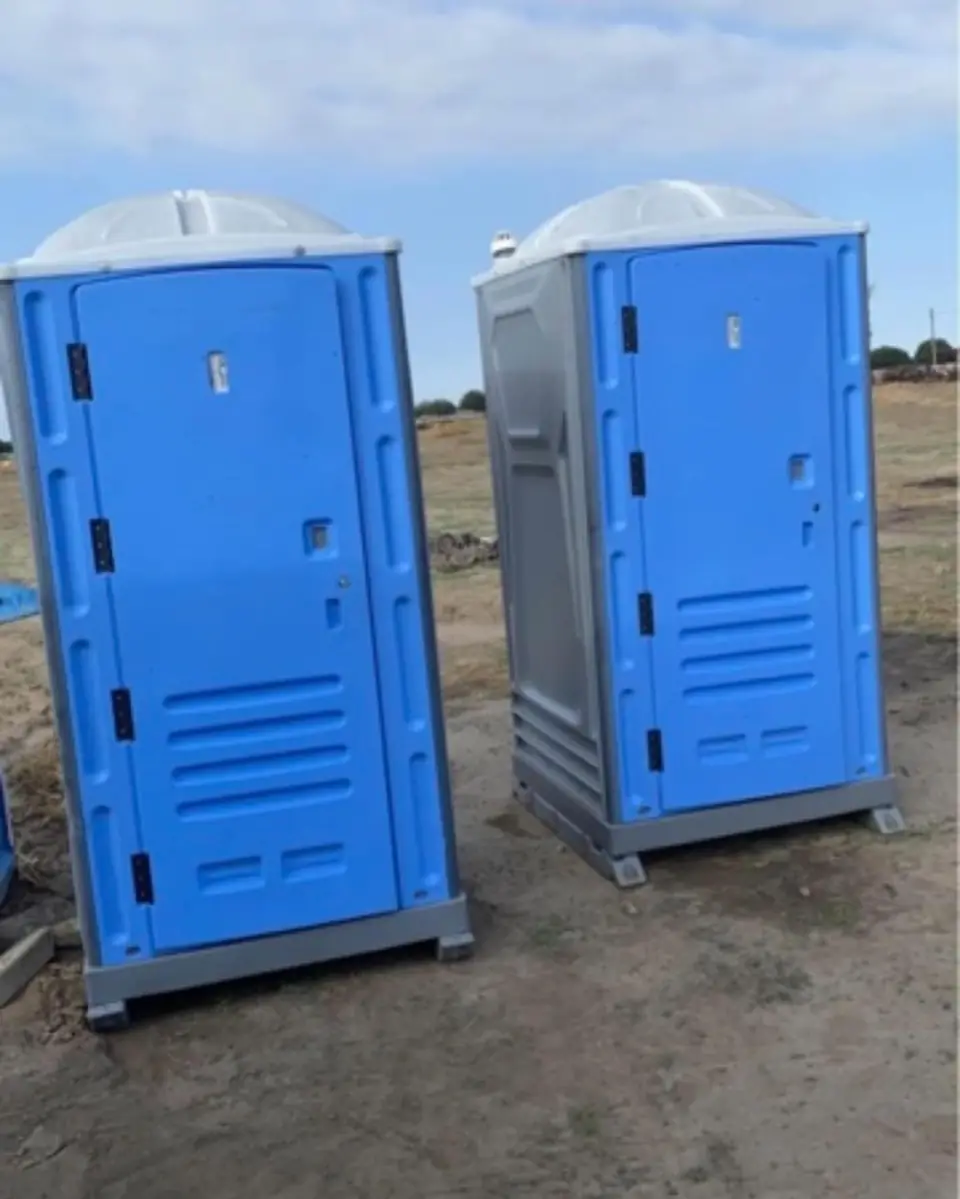 Two blue standard porta potties set on open ground